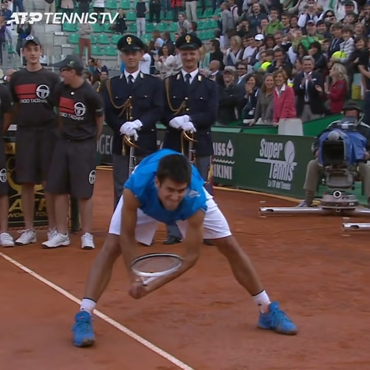 Novak Djokovic bending down to pick up a tennis ball.