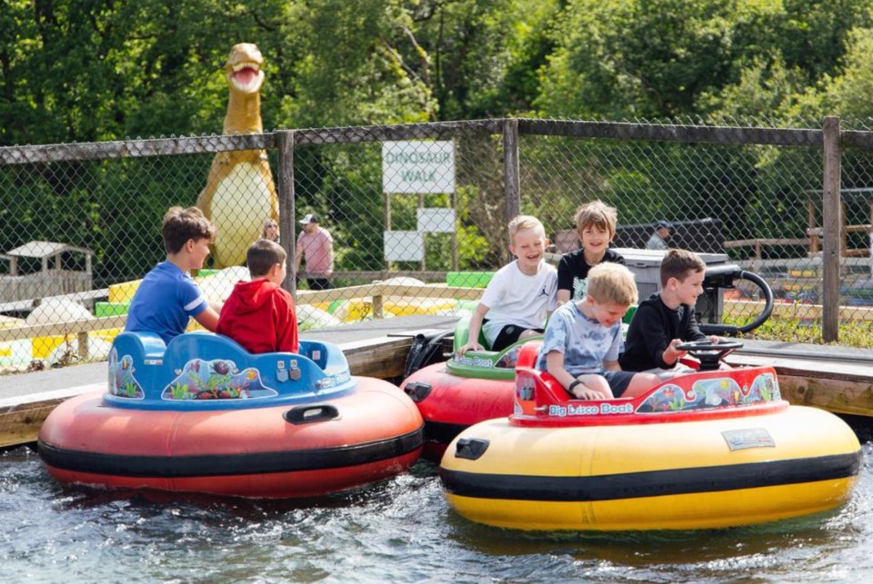 Children enjoying bumper boats at a dinosaur-themed park.