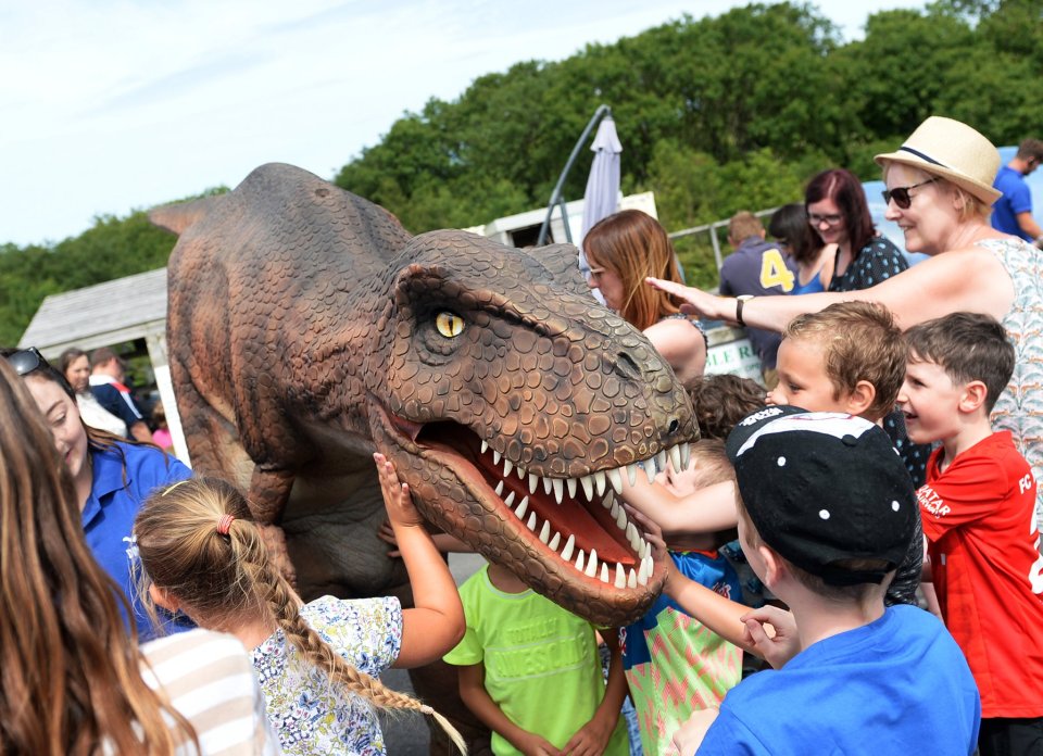 Children interacting with a large animatronic dinosaur at a theme park.