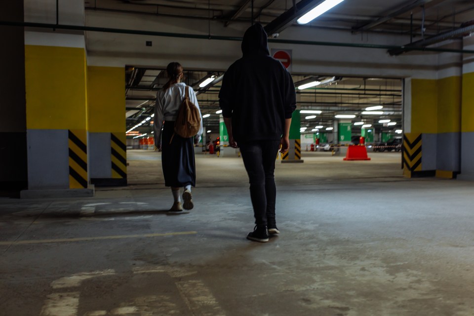 A hooded man following a woman in a parking garage.