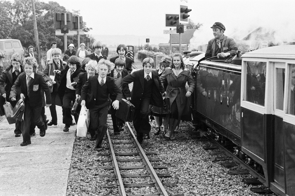 Schoolchildren rush toward a small steam train.