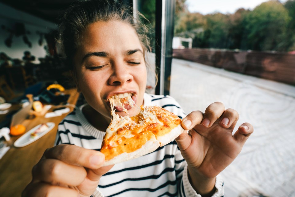 A young woman enjoys eating a slice of pizza.