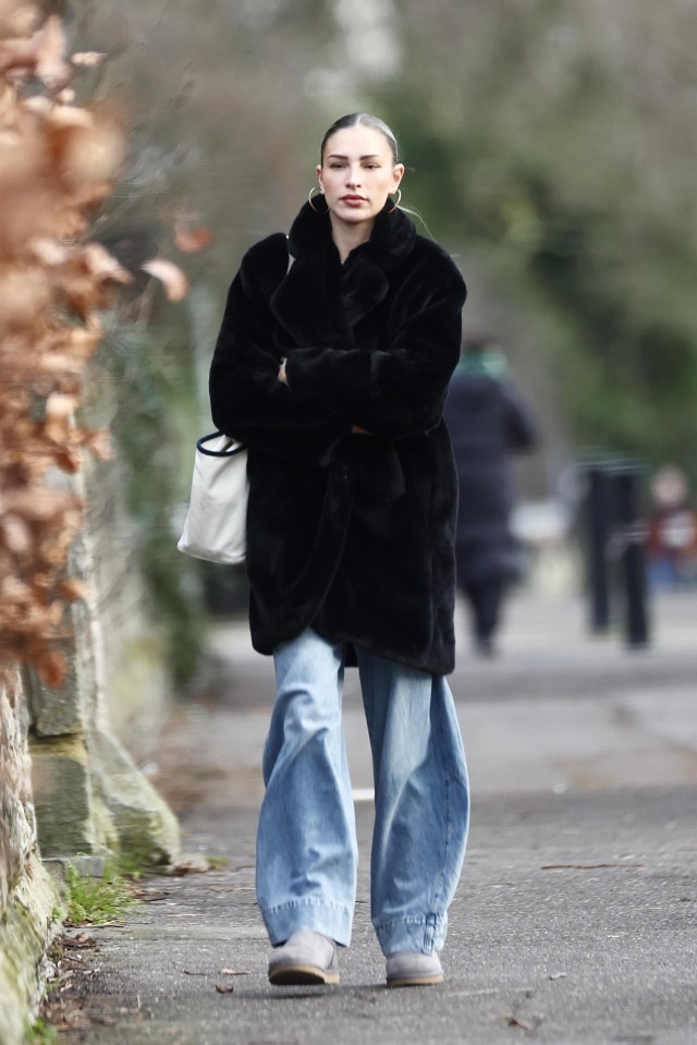 Zara McDermott walking down a street in a black fur coat and blue jeans.