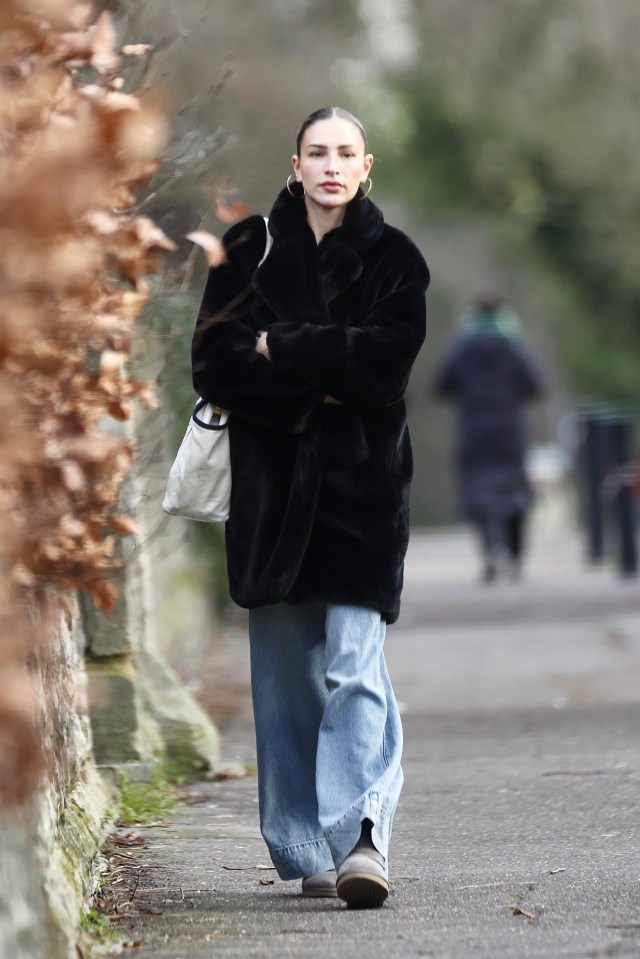 Zara McDermott walking down a street in a black fur coat and blue jeans.