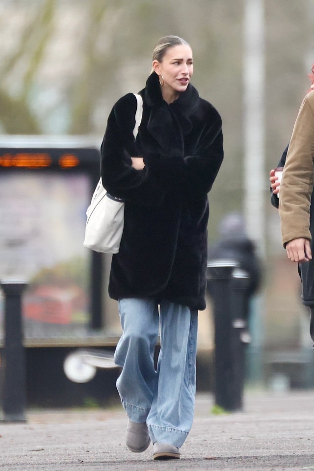 Zara McDermott walking down the street in a black faux fur coat and blue jeans.