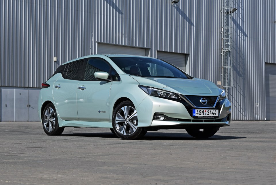 A light green Nissan Leaf electric car parked in front of a building.