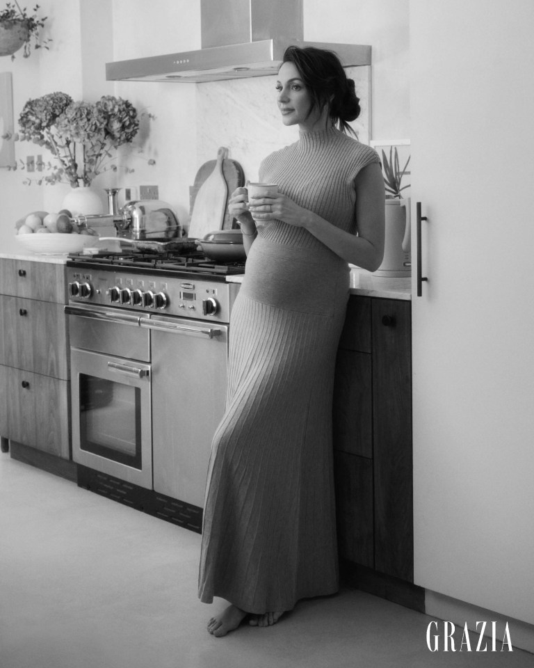 Black and white photo of Michelle Keegan, pregnant, holding a mug in her kitchen.