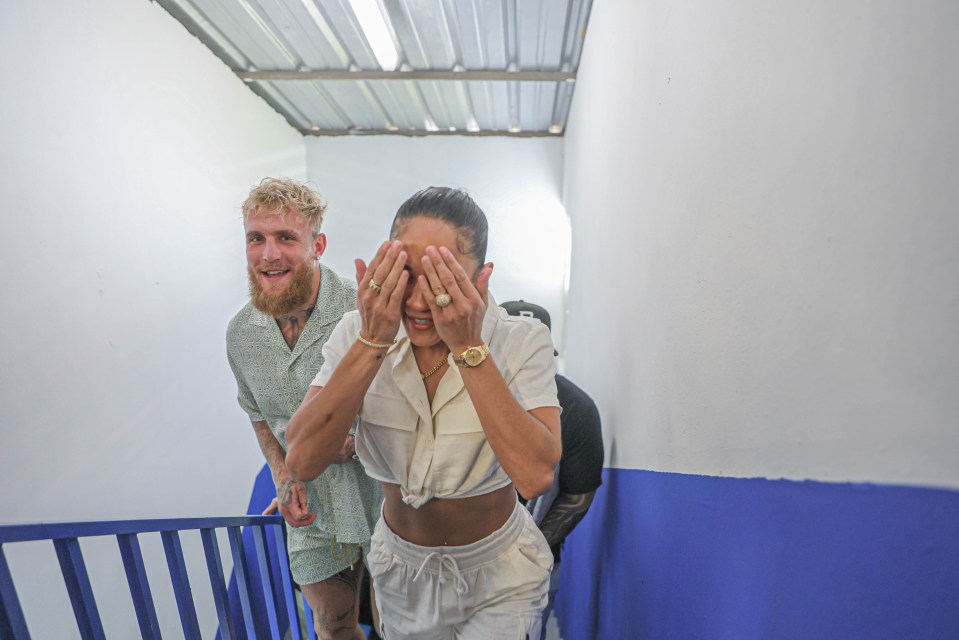 A man and woman walking down a hallway, the woman covering her eyes.