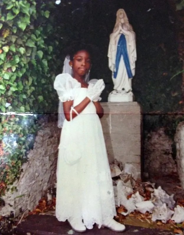 Girl in communion dress praying in front of a statue of Mary.