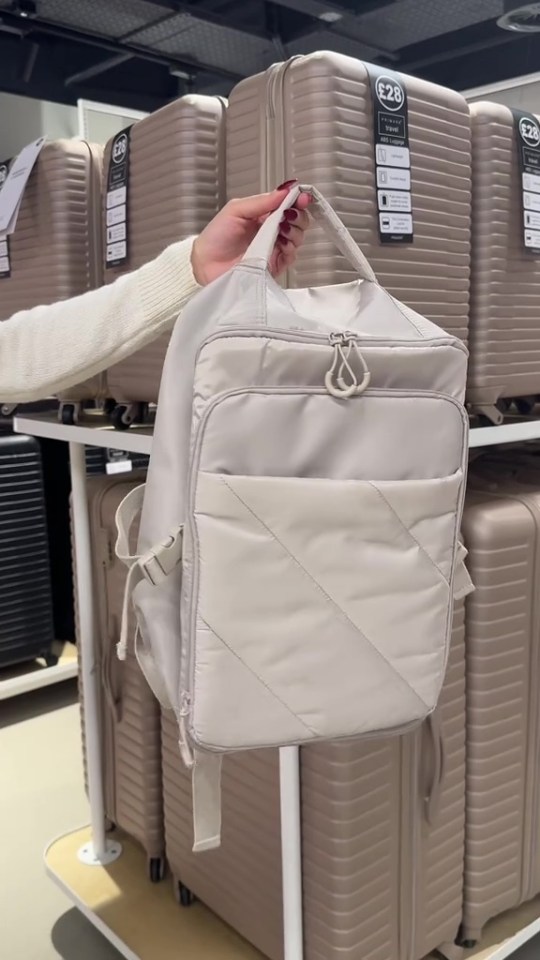 A light beige travel backpack being held in front of several light beige suitcases.