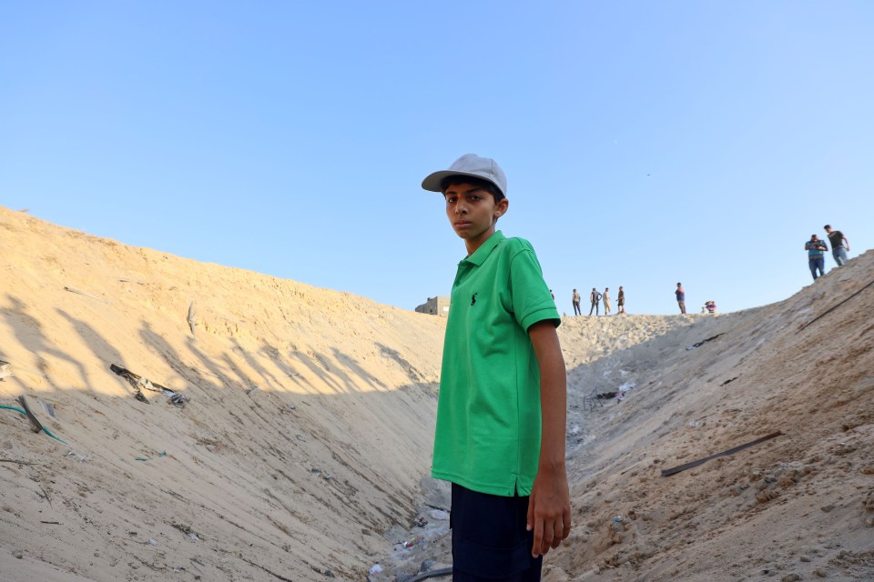 Boy in a green shirt standing in a bomb crater.