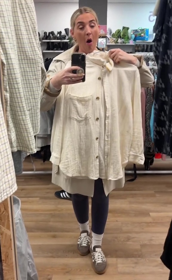 Woman in a charity shop holding up a cream-colored shirt.