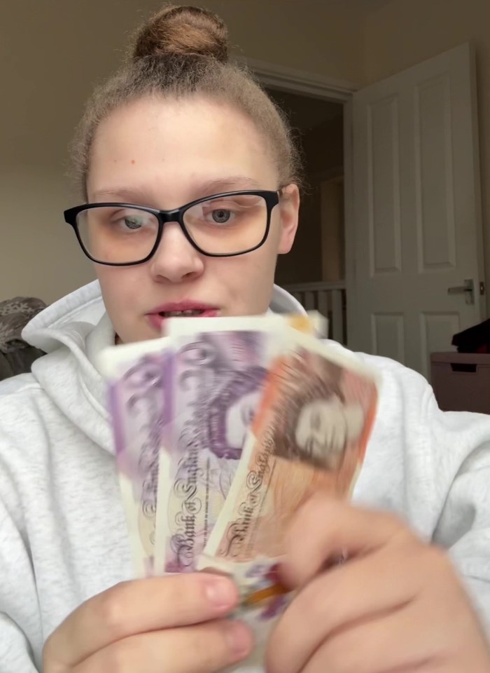 A young woman holds up fifty British pounds, expressing concern about the amount for three weeks with three children.