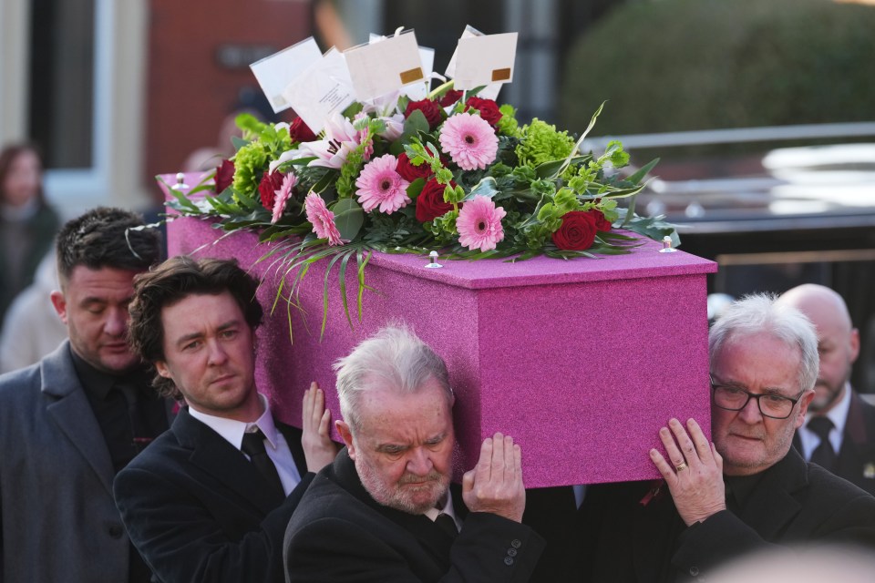 Pallbearers carrying a pink coffin adorned with flowers.