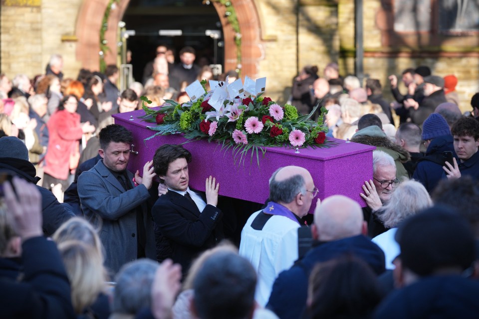 Mourners carrying a pink coffin at a funeral.