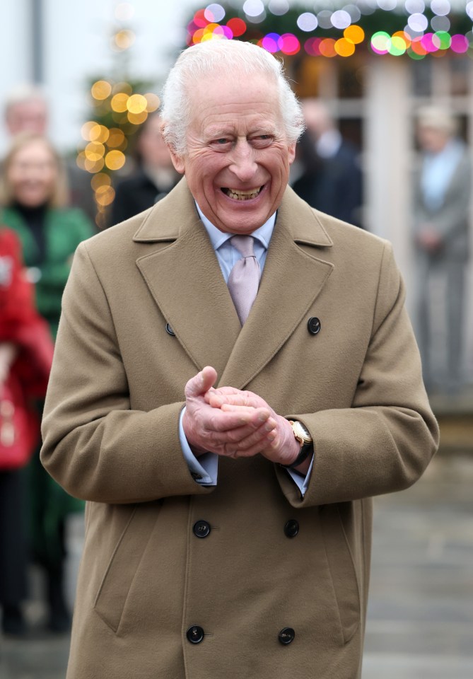 King Charles III smiling and clapping at a Christmas event.