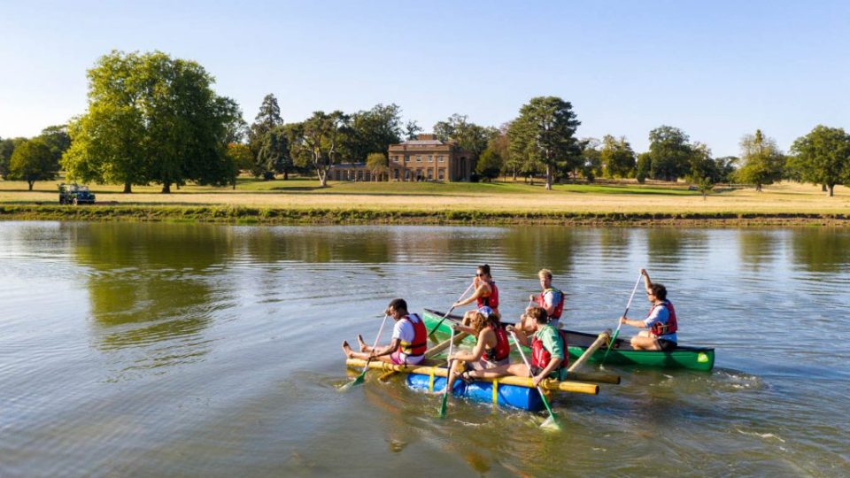 Group of people rafting on a lake in front of a manor house.