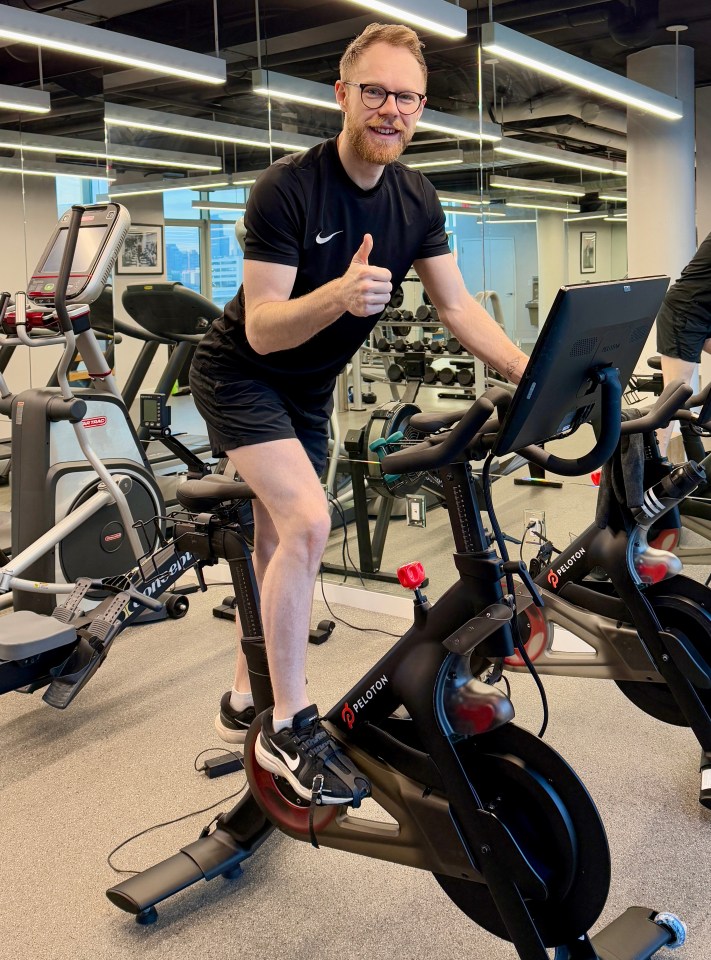 Man giving thumbs up while using a Peloton stationary bike in a gym.