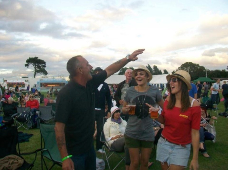 Man pointing with daughters at outdoor event.