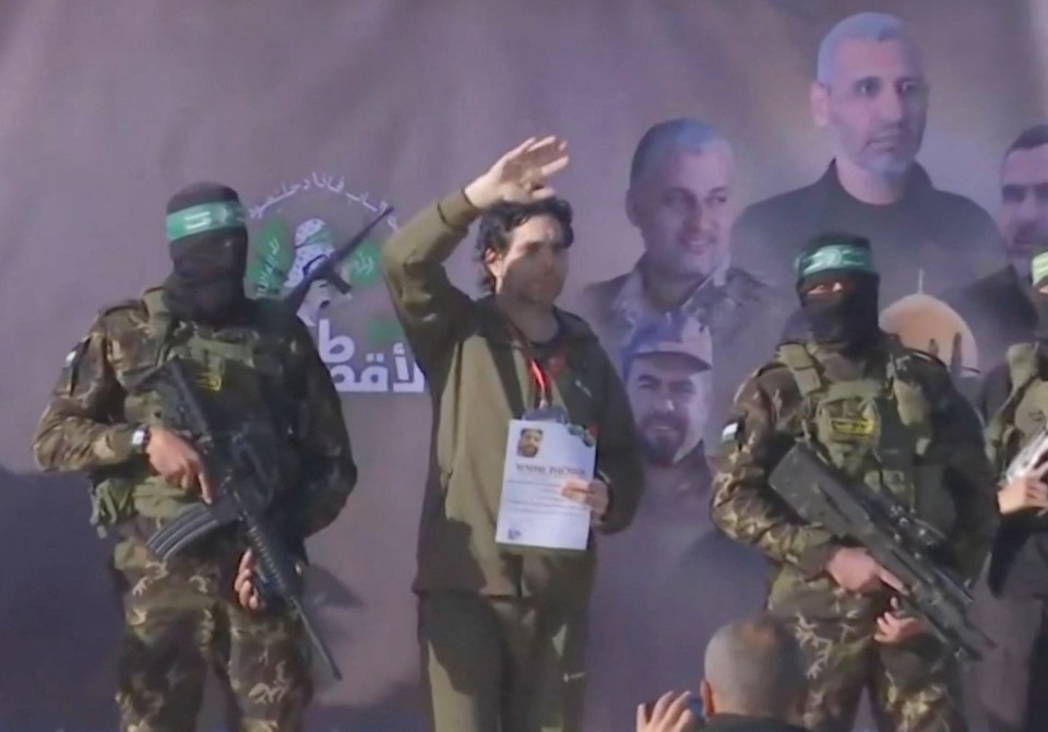 Released hostage waving, flanked by Hamas militants with rifles.