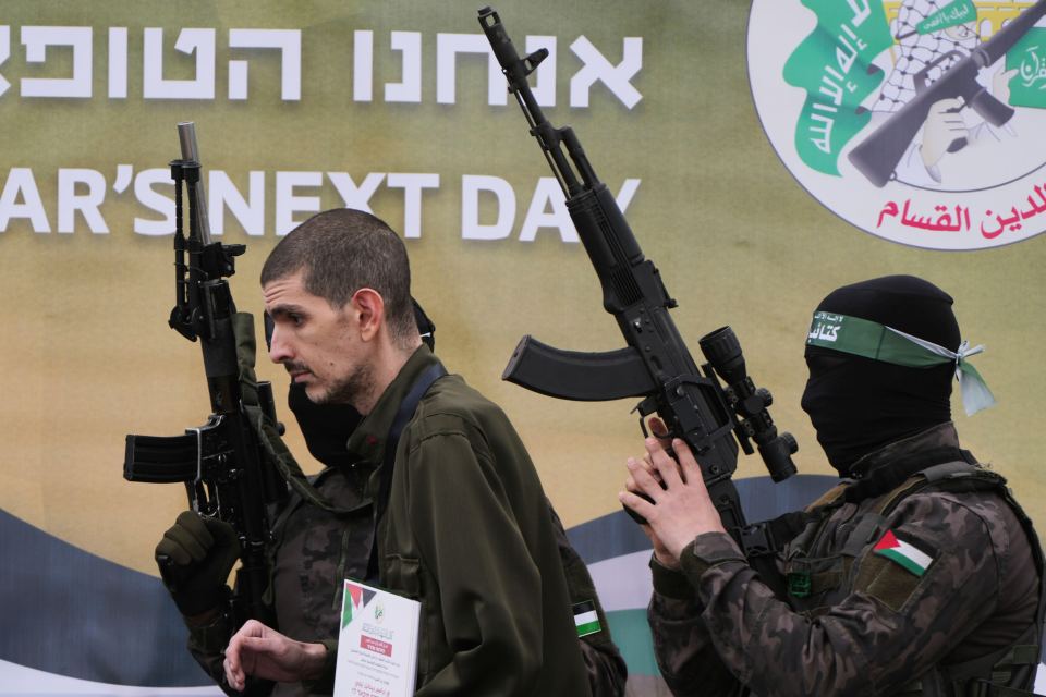 Man in military uniform being interviewed by armed men.