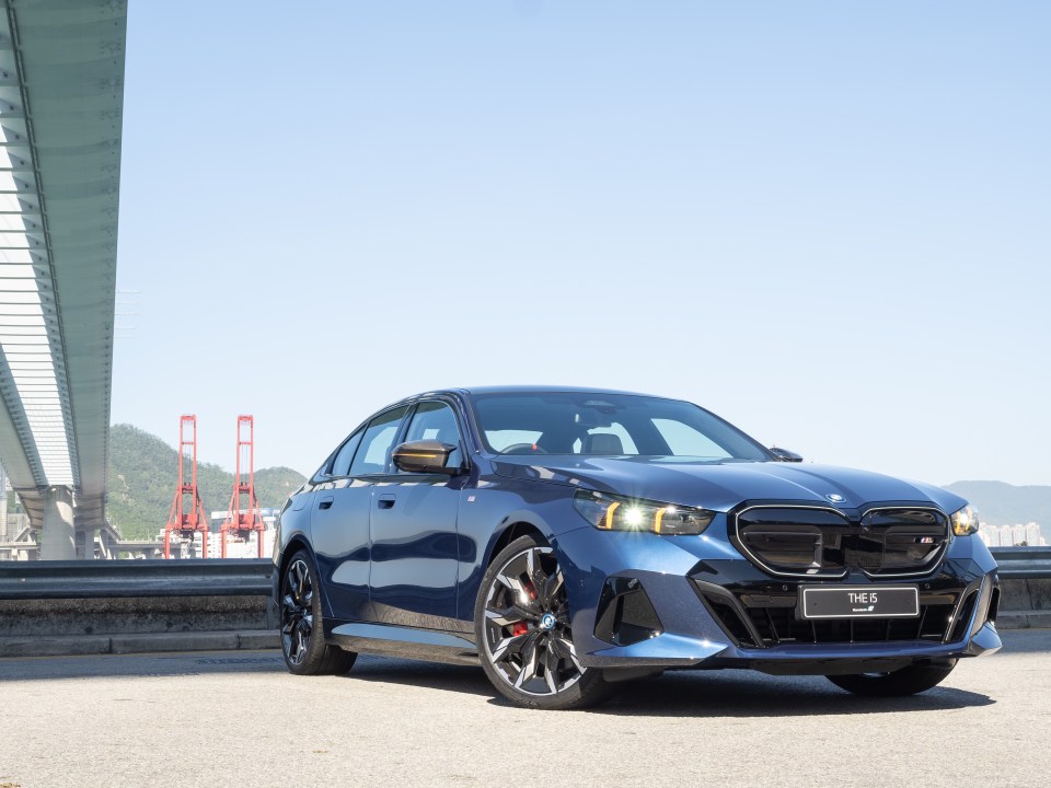 A dark blue BMW i5 parked near a bridge.