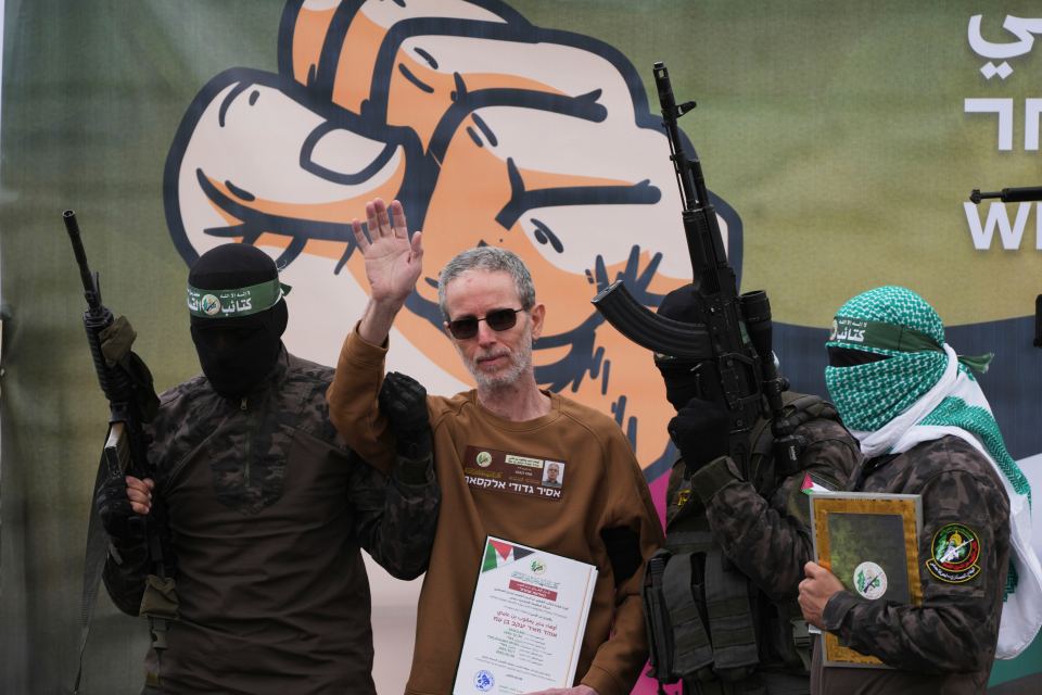 A man in a brown sweatshirt stands surrounded by armed militants.