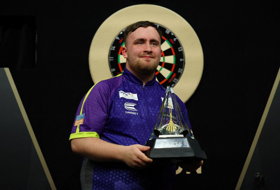 Luke Littler holding a darts trophy.