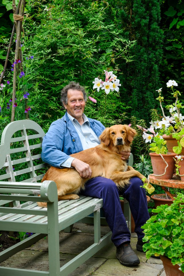 Monty Don sitting on a bench in a garden with his dog.