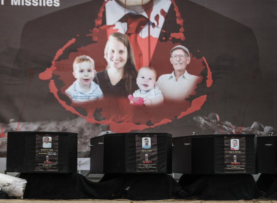 Four caskets containing the bodies of Israeli victims, displayed with photos and information about the deceased and accusations against the Israeli Prime Minister.