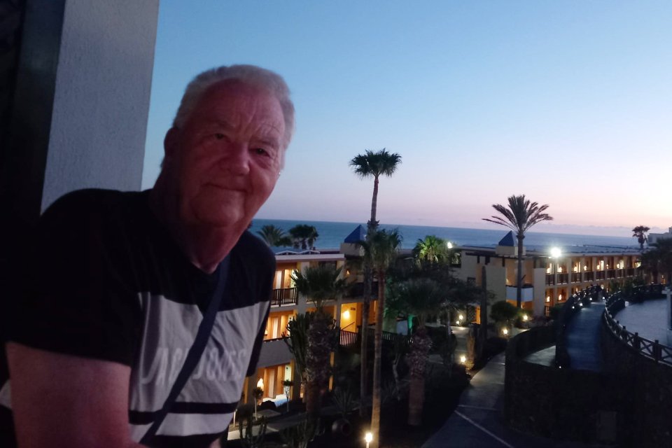 A man on a balcony overlooking a resort at dusk.