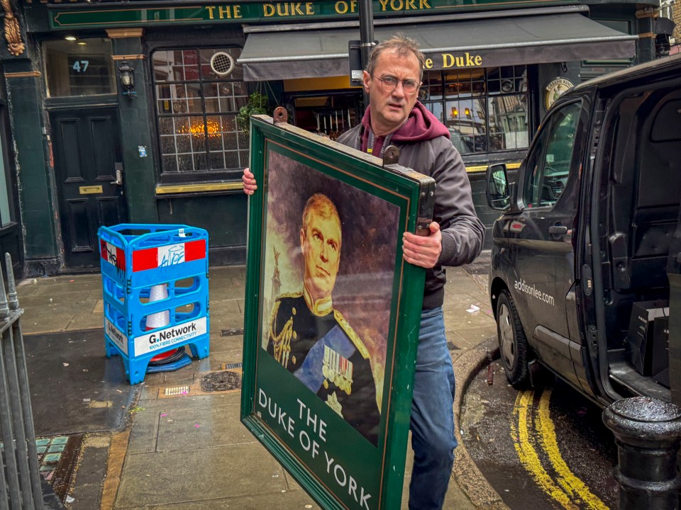 Man carrying pub sign with Prince Andrew's portrait.