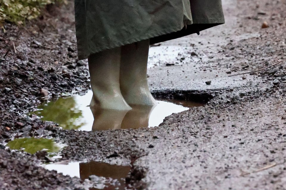 Person's legs in rain boots standing in a pothole.