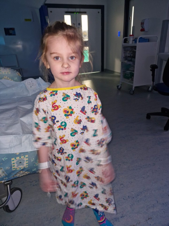 A five-year-old girl in a hospital gown.