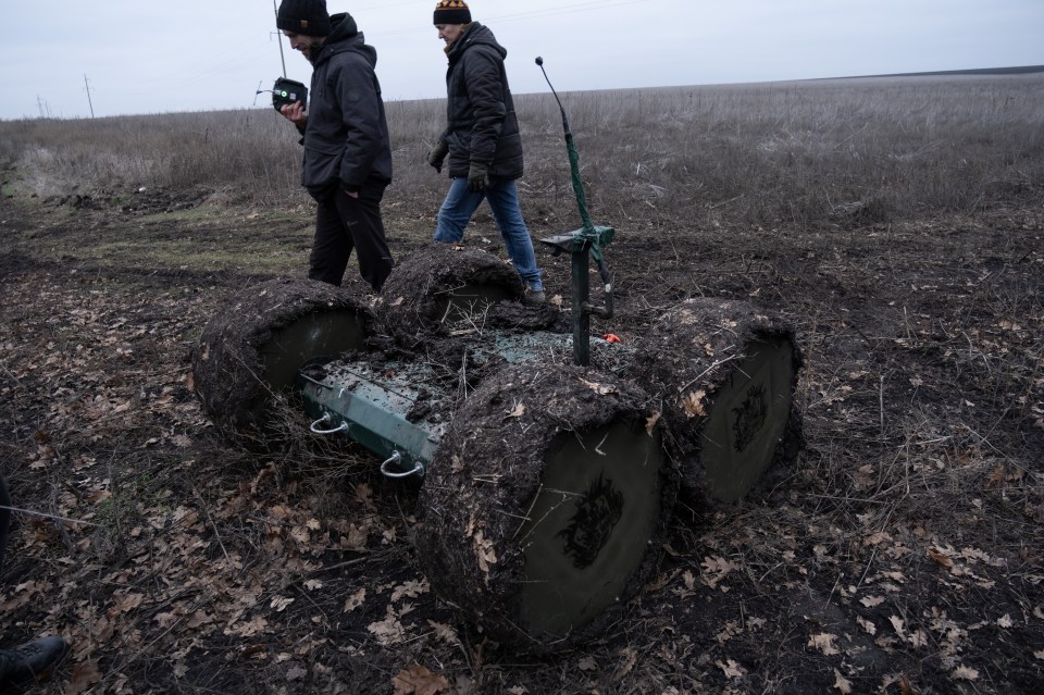 A mud-covered ground drone being operated by two soldiers in a field.