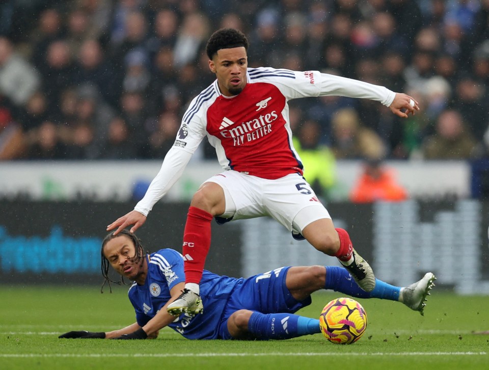 Soccer player in red jersey tackles player in blue jersey.