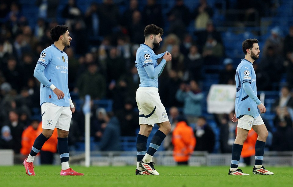 Three dejected Manchester City soccer players on the field after a match.