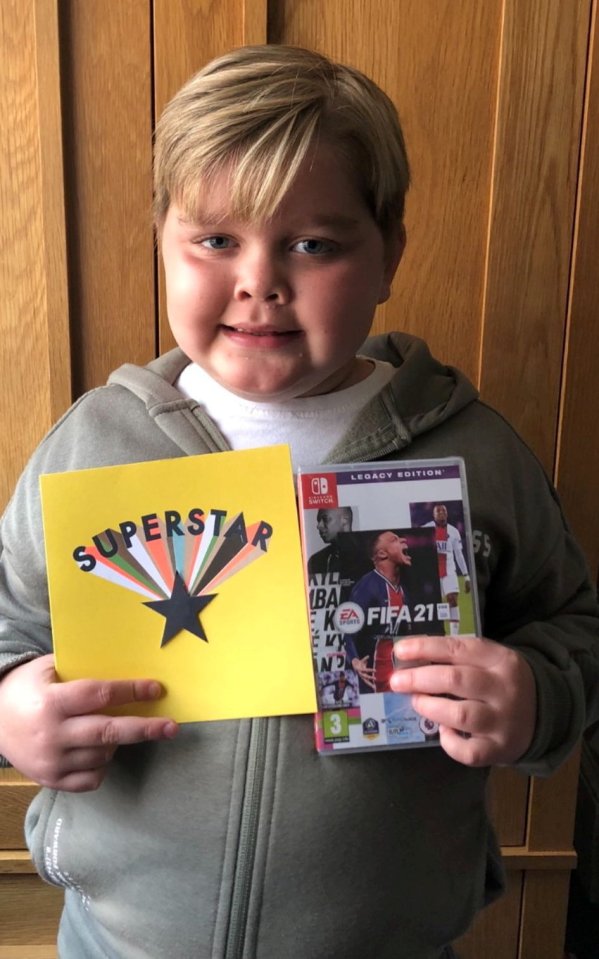 Boy holding a card that says "Superstar" and a FIFA 21 video game.