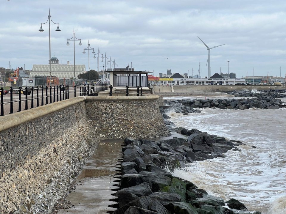 Lowestoft seafront with waves crashing against rocks and a sea wall.