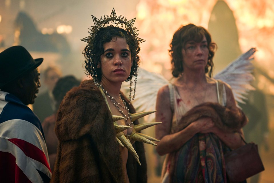 Two women in elaborate costumes, one wearing a crown and fur stole, the other with wings, stand against a fiery background.