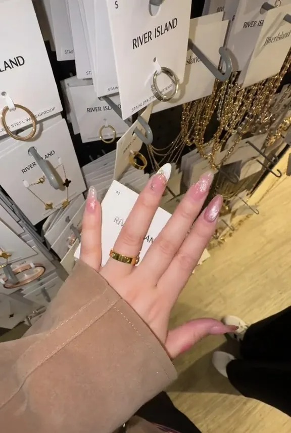 Hand wearing a gold ring in front of River Island jewelry displays.