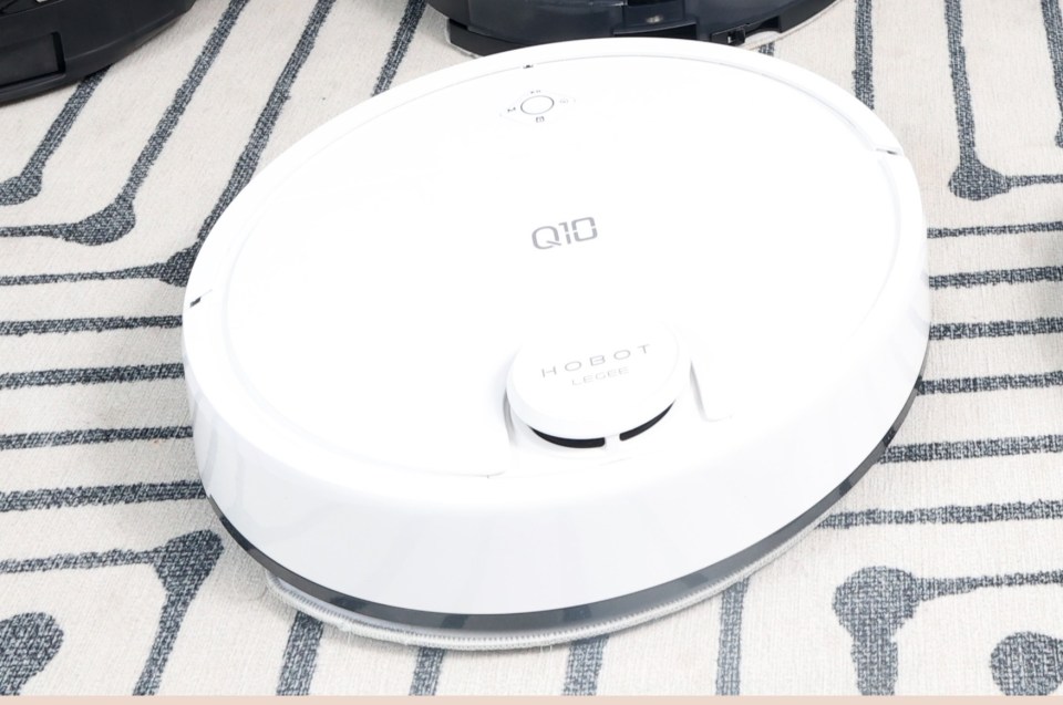 Woman relaxing on a couch with several robot vacuums on the floor.