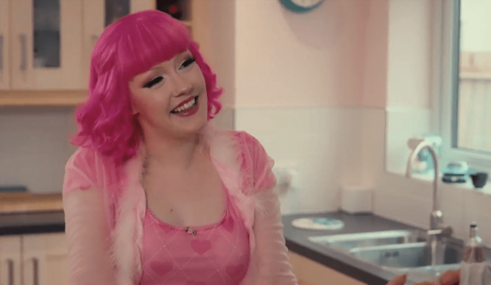 Woman with pink hair smiling in a kitchen.