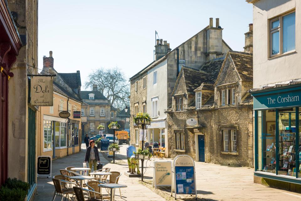 Sunny street scene in Corsham, England, with shops and outdoor seating.