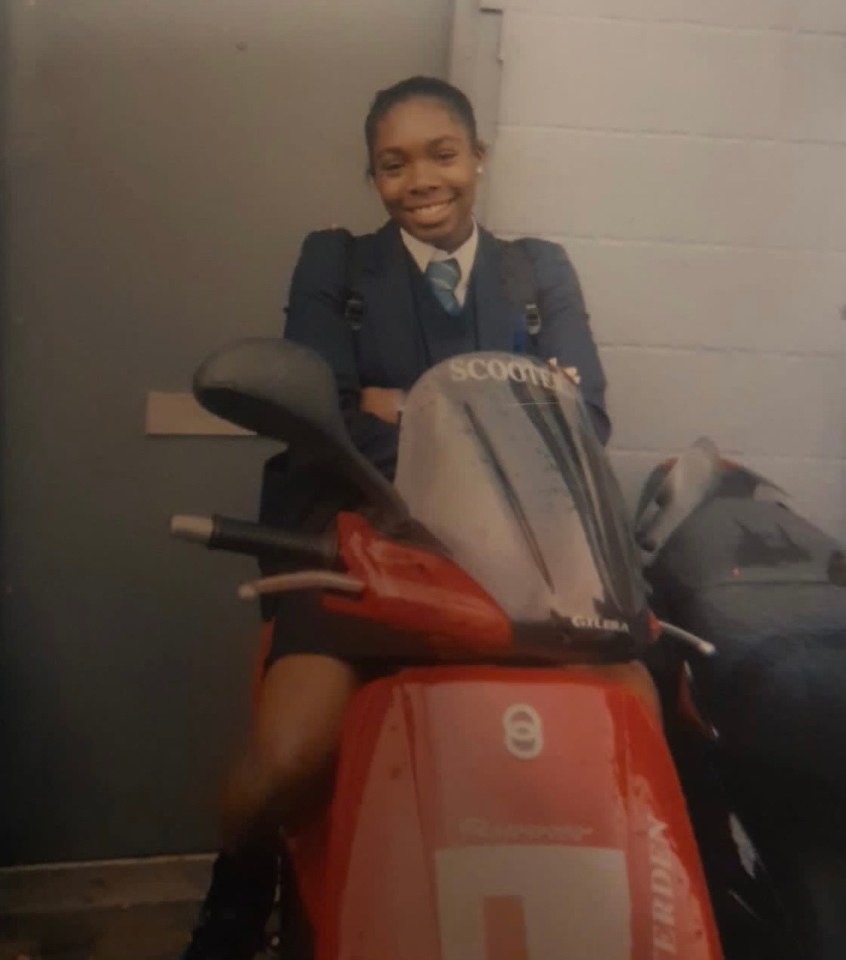 A girl in a school uniform sits on a red scooter.