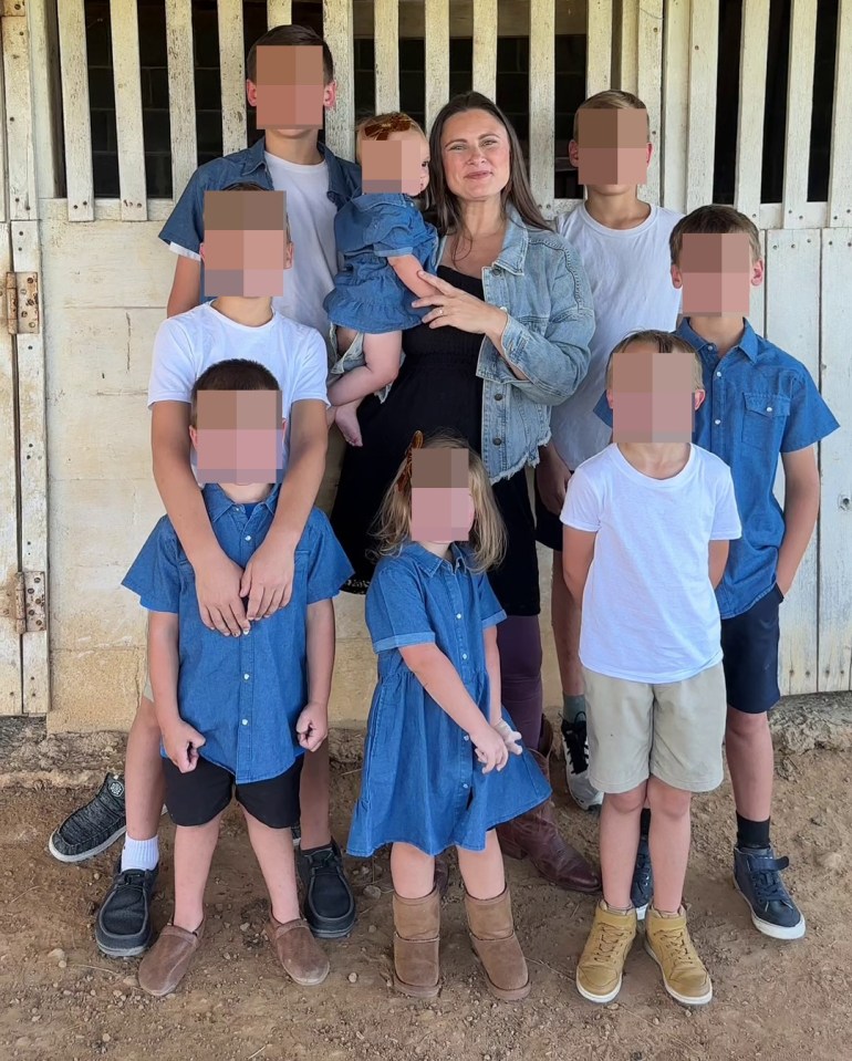 A mother of eight children poses for a photo with her family.  The children's faces are blurred.