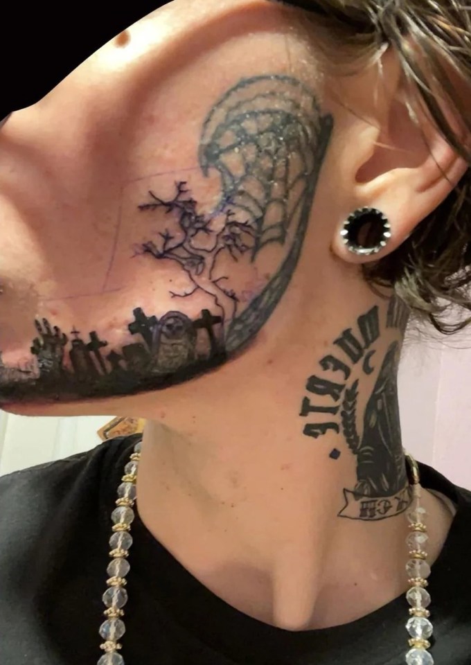 Person's face and neck with several tattoos, including a graveyard scene on their jawline.