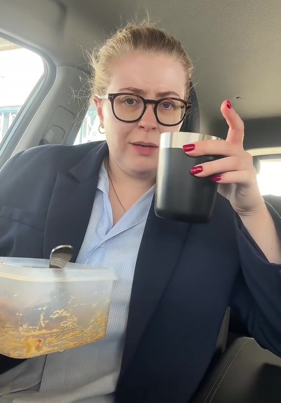 Woman in a car holding a container of food and a drink.