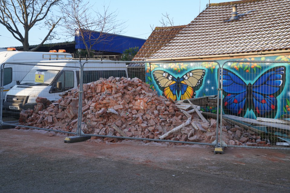 Debris pile behind a temporary fence in front of a building with a butterfly mural.