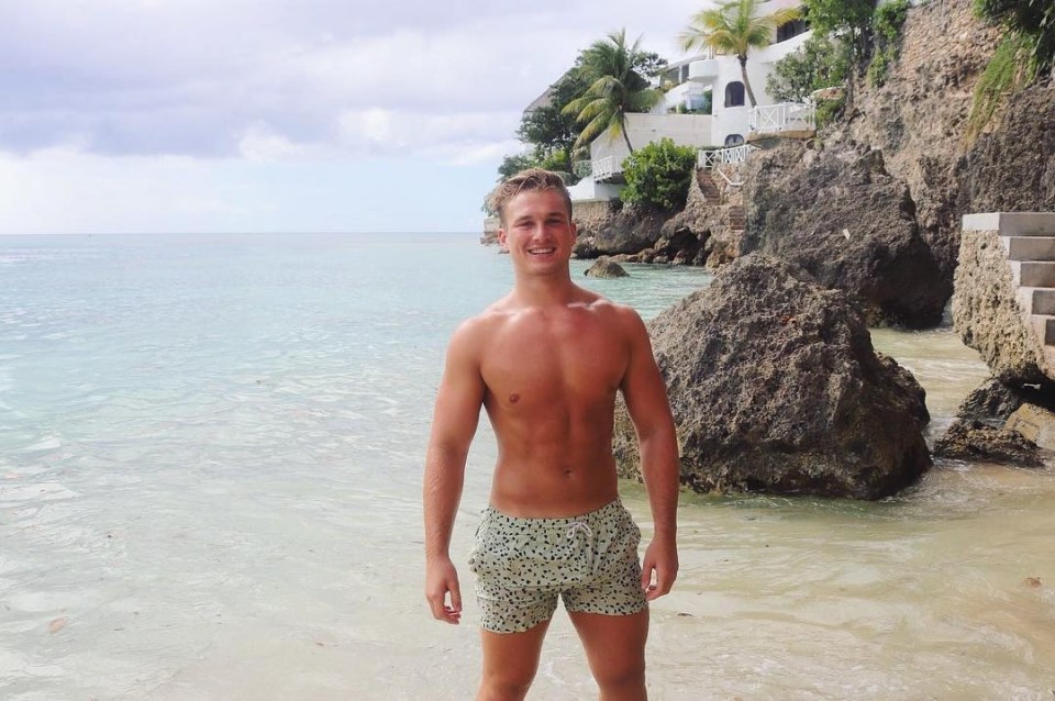 Man in swim trunks smiling on a beach.